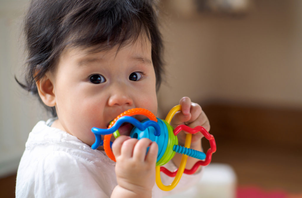 Teething baby using a rainbow teething toy.
