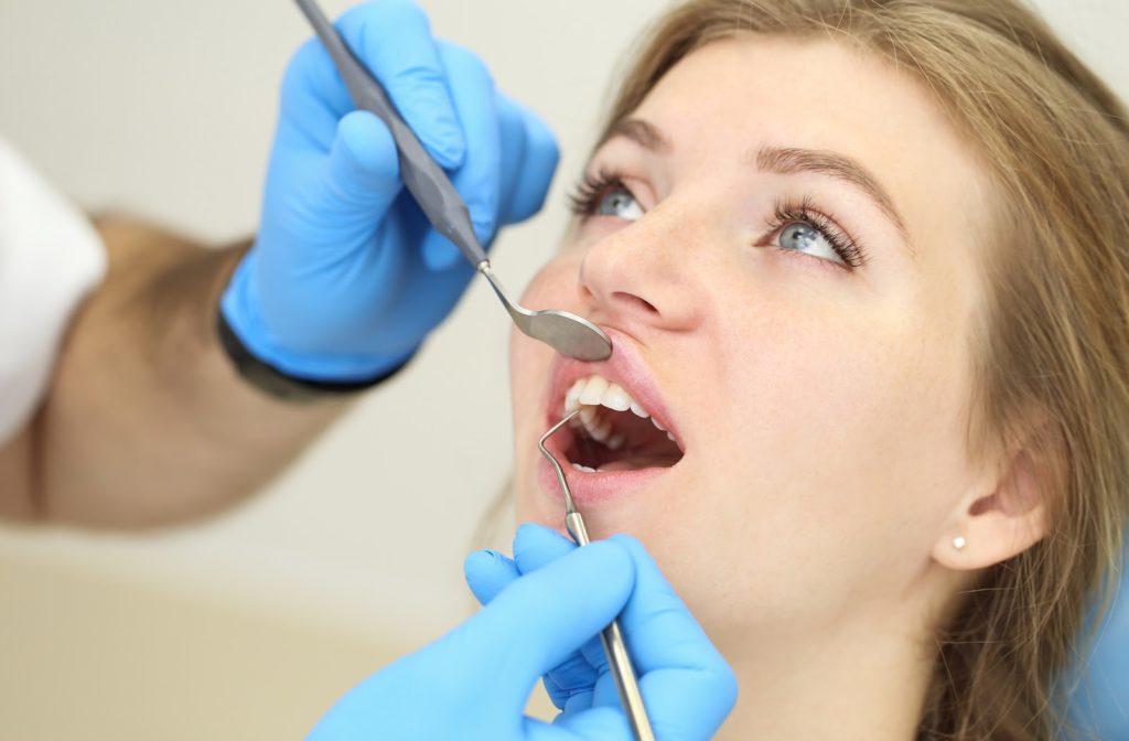 blonde woman undergoing a dental exam with a dentist looking in her mouth using a scaler and dental mirror