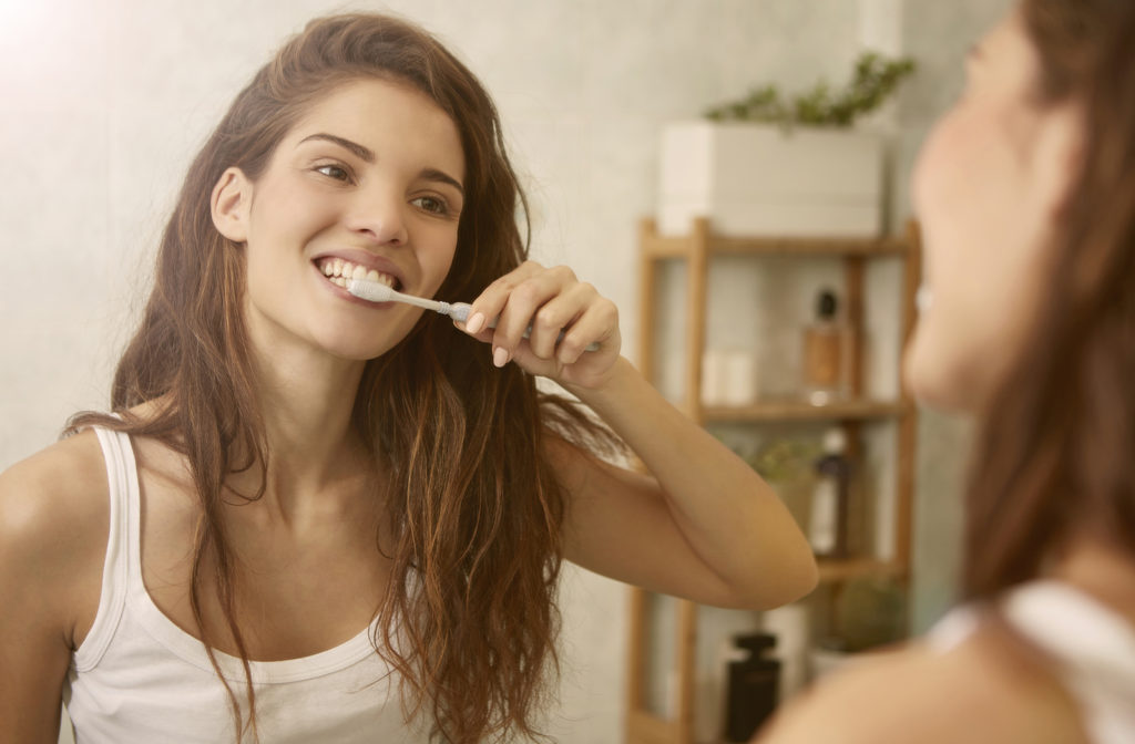 Young women brushing teeth while looking in mirror at home