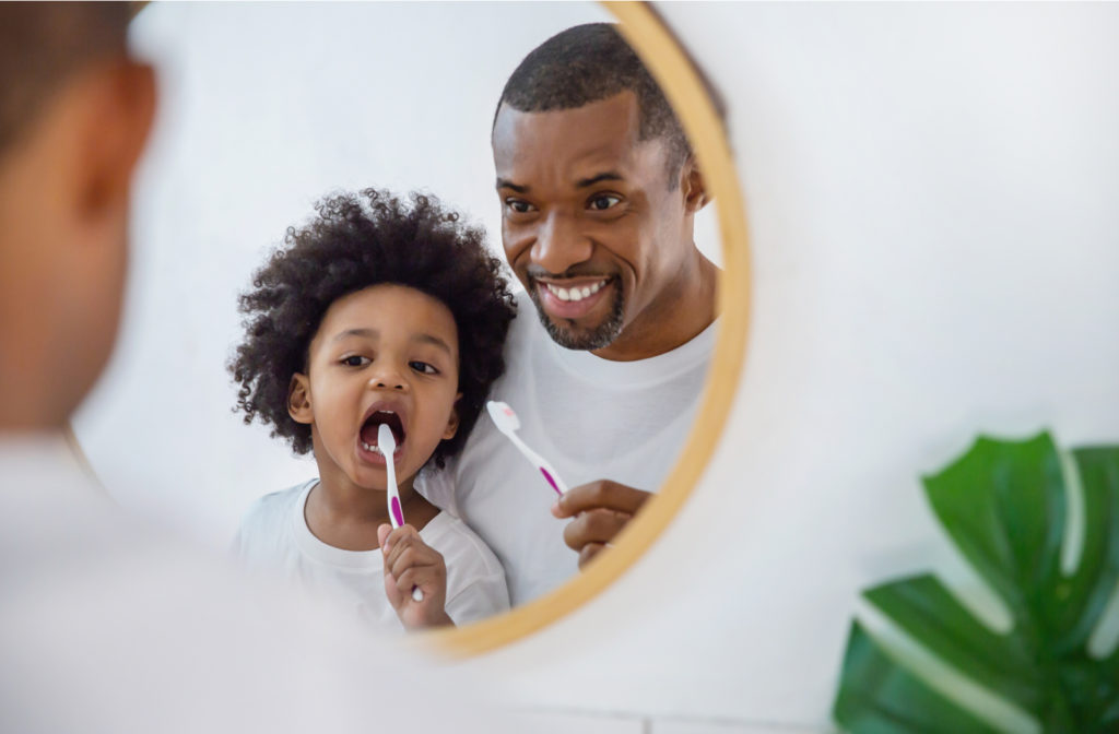 Father and son brushing teeth together while looking in mirror