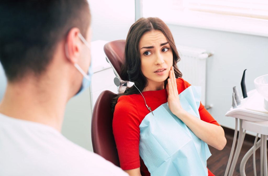 alt text: A woman holding the side of her face due to mouth pain, talking to her dentist